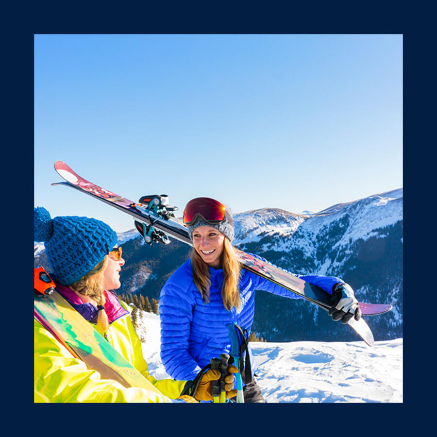 2 women on snowy mountain carrying skiis